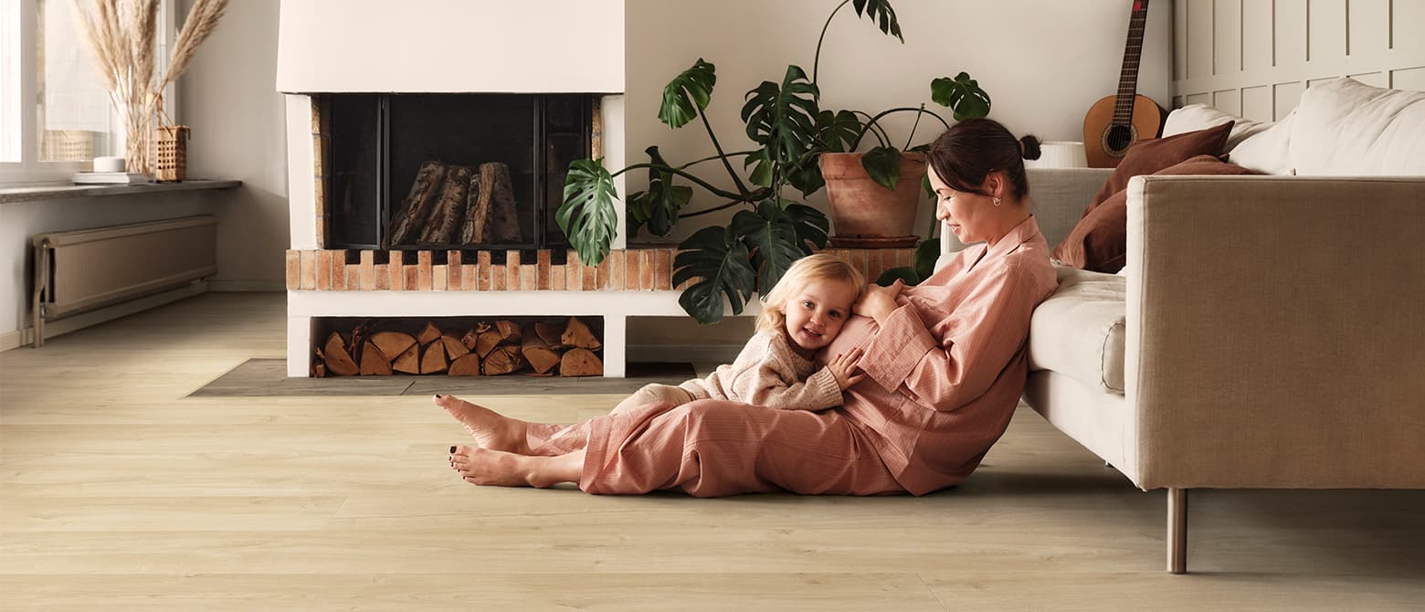 gravid kvinna och dotter sitter på ett beige laminatgolv i ett vardagsrum
